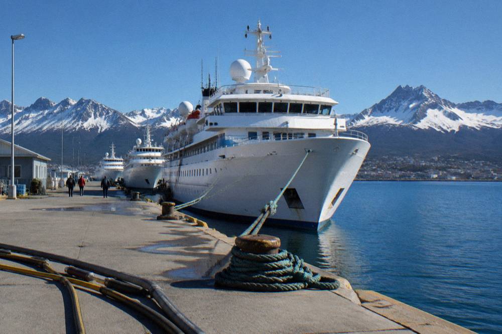 Three expedition ships at a dock in a southern port town with mountains behind