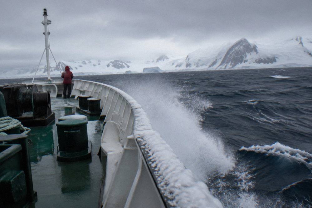 Expedition ship bow cutting through open ocean swell under a grey sky