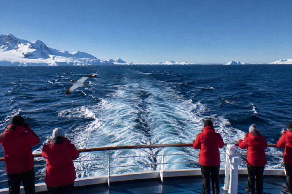 Passengers in red parkas watching seabirds from an expedition ship deck