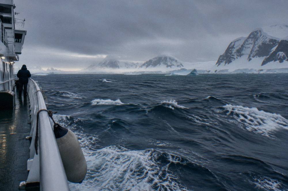 Expedition ship moving through moderate open ocean swell with whitecaps under a grey sky