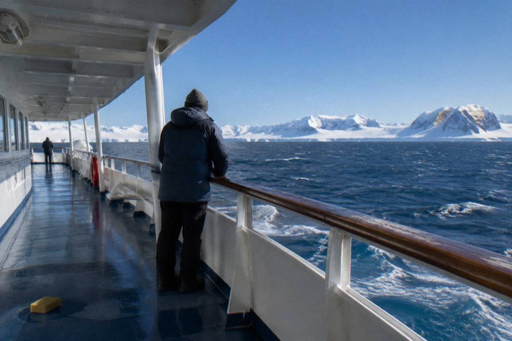 Traveller in warm jacket standing at an open deck rail looking at the horizon over open sea