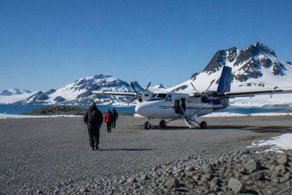 A twin-engine aircraft on a gravel airstrip surrounded by snowy Antarctic mountains
