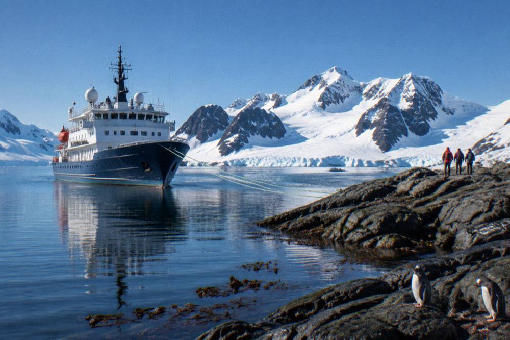 A modern small expedition ship moored beside a rocky Antarctic shoreline