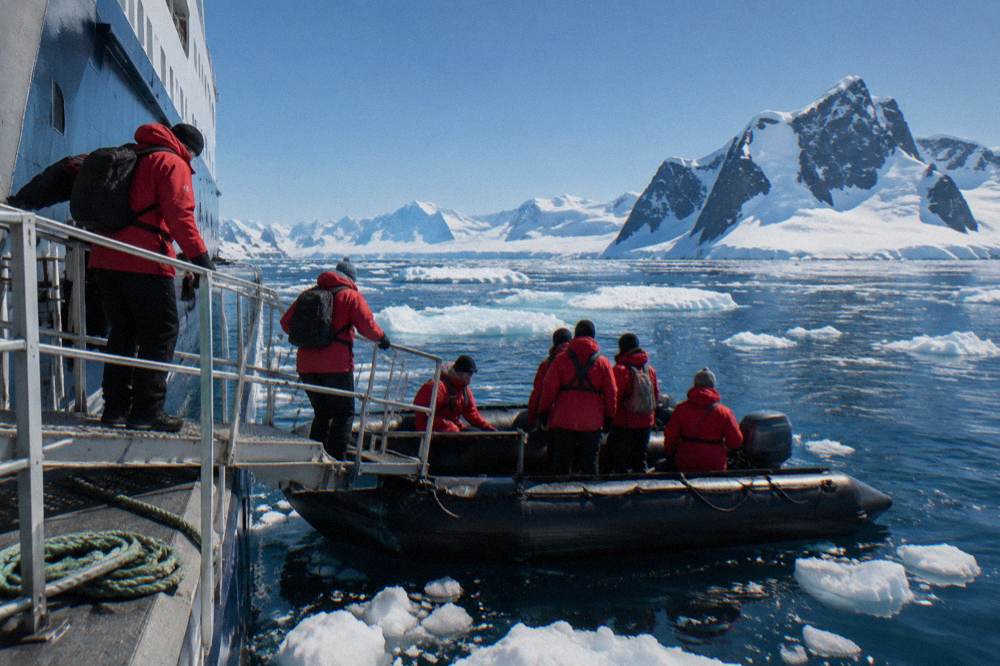 Passengers in red parkas boarding a small boat from an expedition ship in icy water