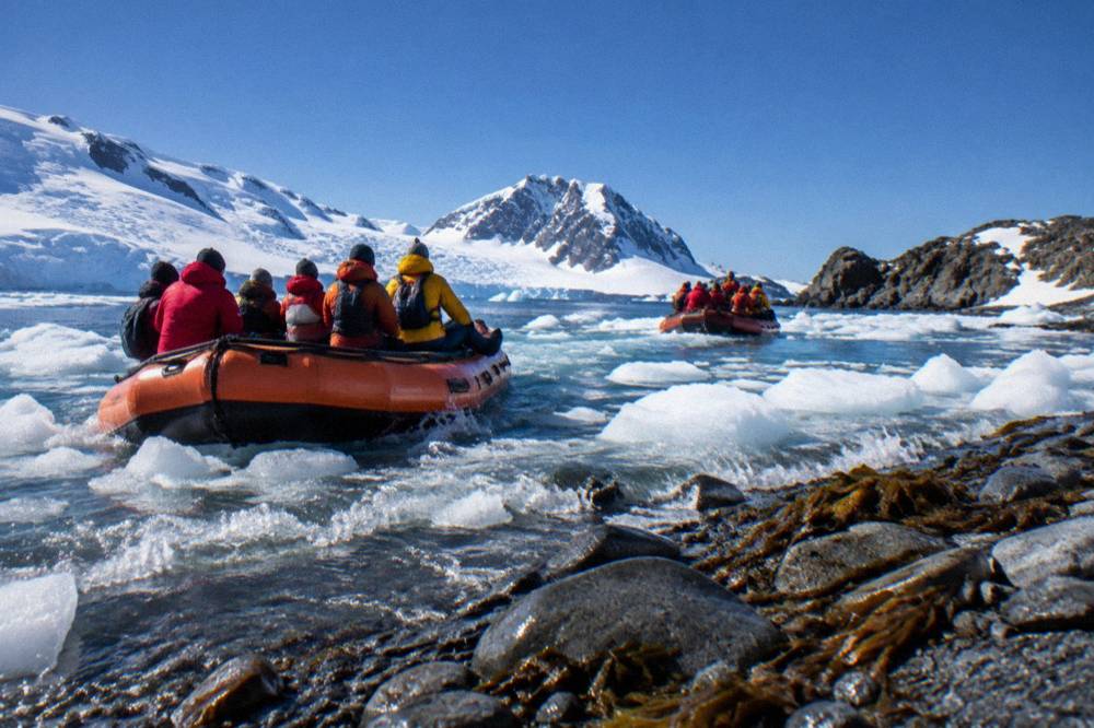 Two orange Zodiacs carrying passengers through brash ice toward a rocky shoreline