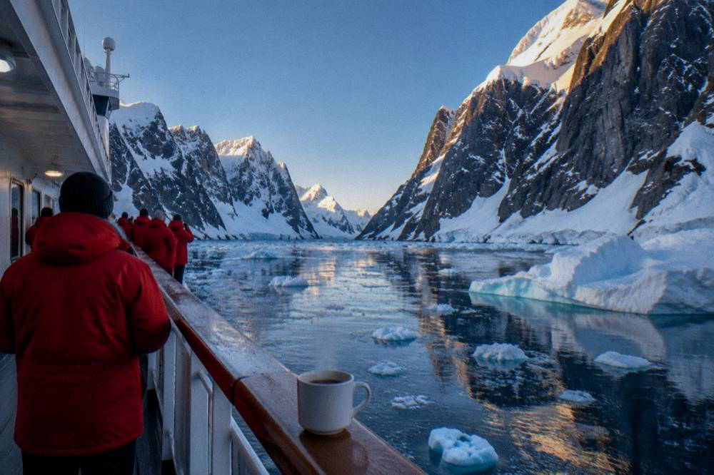 Passengers in red parkas standing along a ship's deck watching glaciers pass
