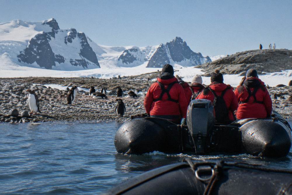 Passengers in red parkas watching penguins from a Zodiac