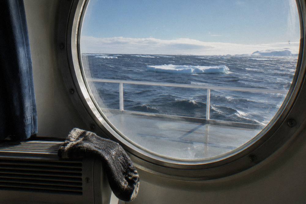 Expedition ship cabin porthole with sea ice visible beyond the window