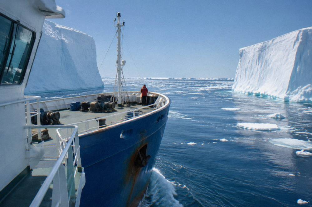 Small expedition ship sailing between icebergs near the Antarctic Peninsula