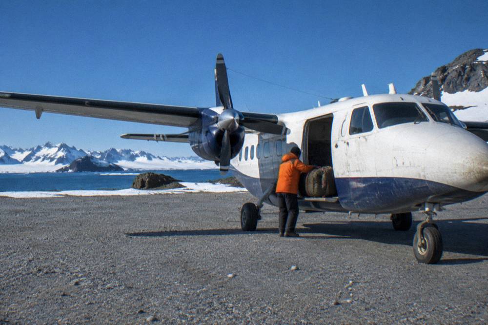 A small twin-engine charter aircraft on a gravel airstrip on King George Island in Antarctica.