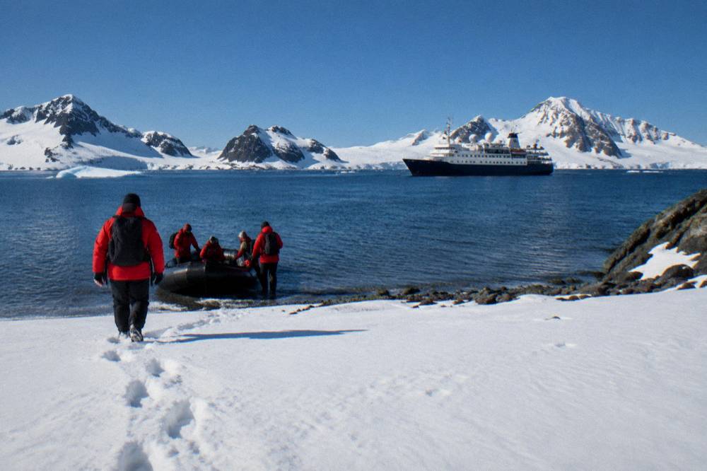 Passengers in red parkas boarding a Zodiac from an expedition ship in an Antarctic bay.