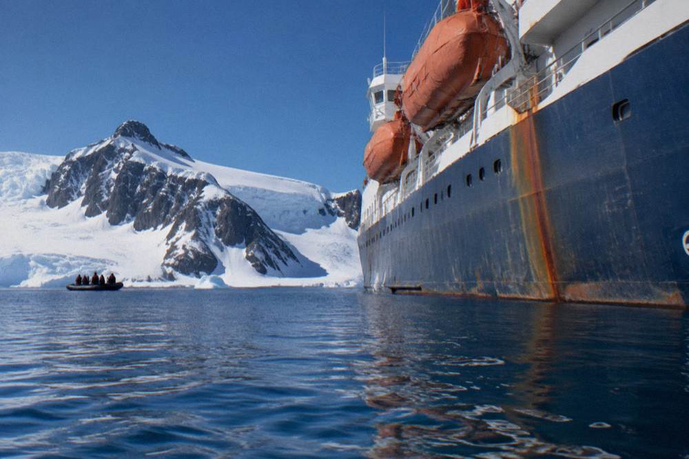 Ice-strengthened expedition ship anchored near snow-covered Antarctic coastline