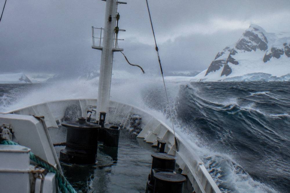 Bow of an expedition ship with an inverted hull design pushing through a wave
