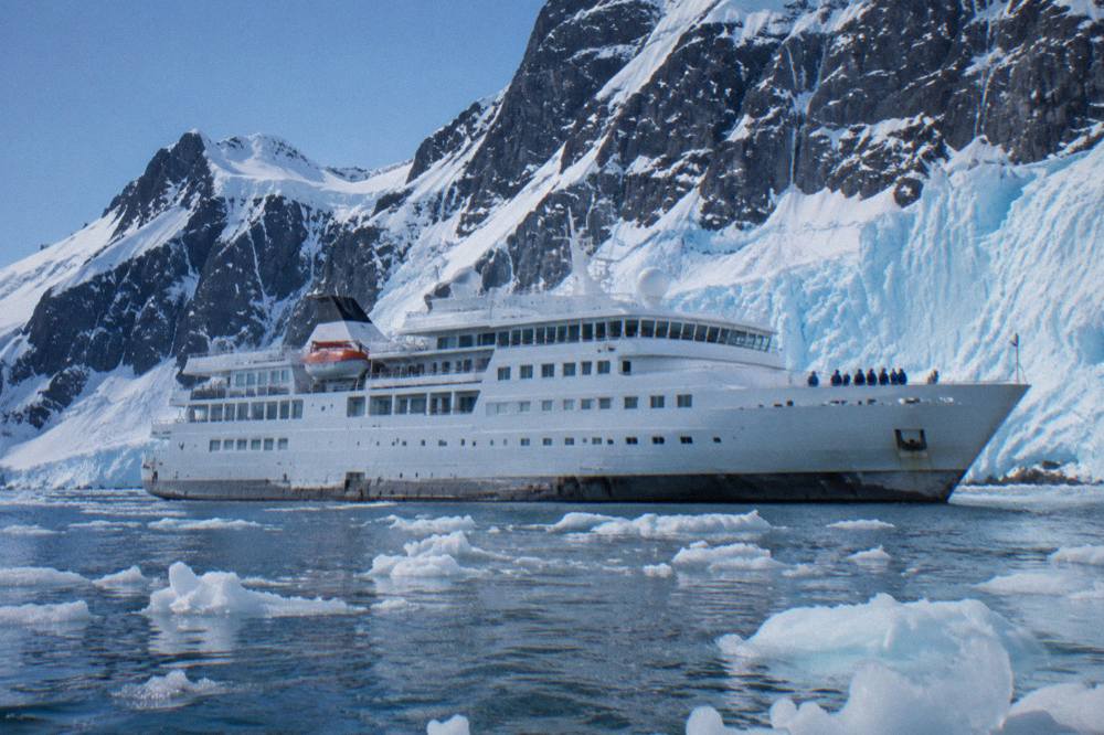 Small luxury expedition ship cruising past a wall of Antarctic ice