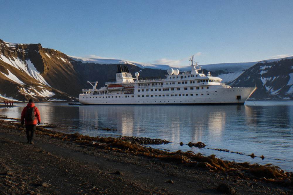 Luxury expedition ship at anchor in a calm Antarctic bay at golden hour