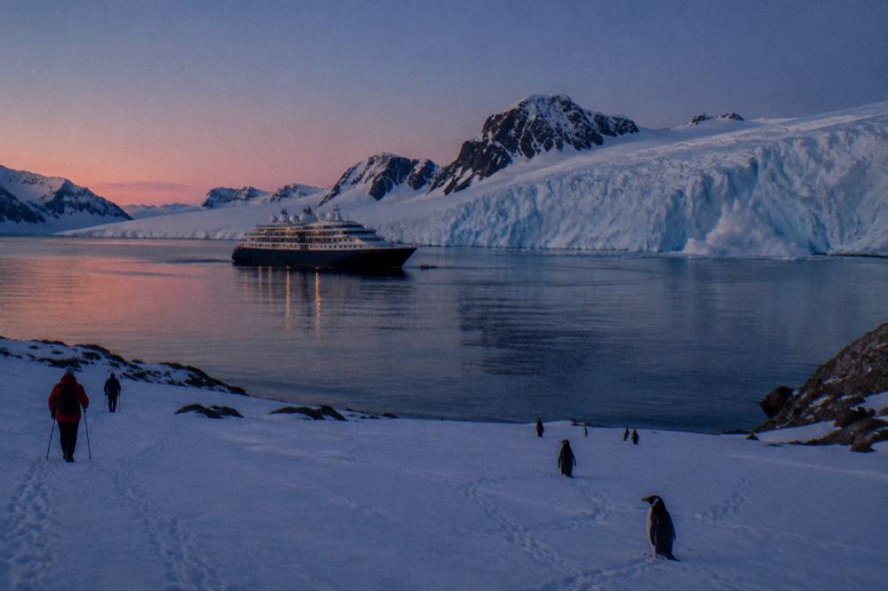 A luxury expedition ship at anchor in a calm Antarctic bay at dusk