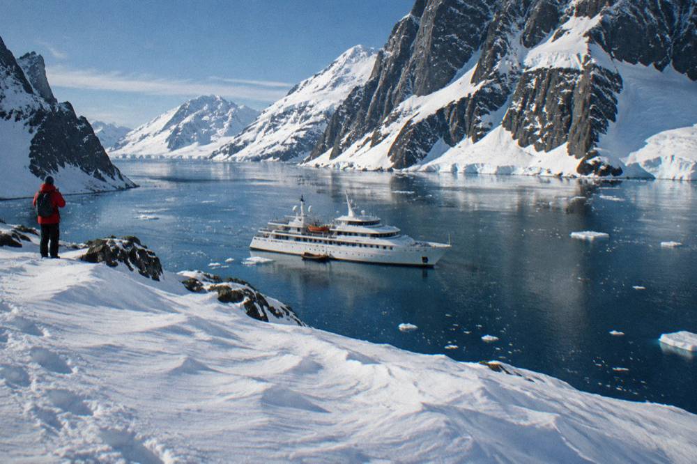 Expedition yacht anchored in a calm channel between snow-covered Antarctic peaks