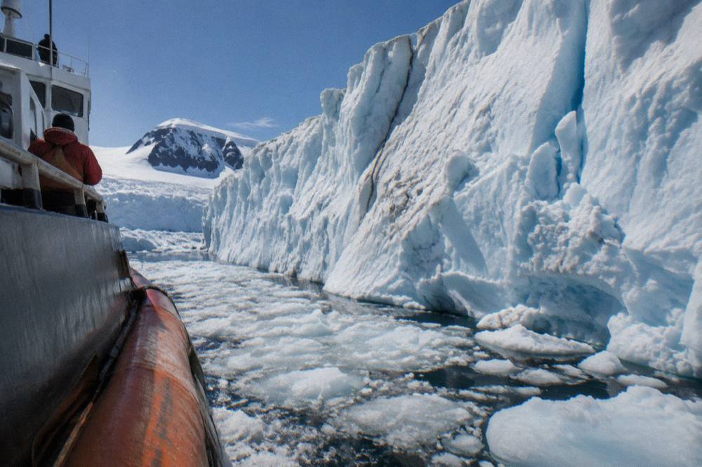 Small expedition ship cruising past a wall of Antarctic ice