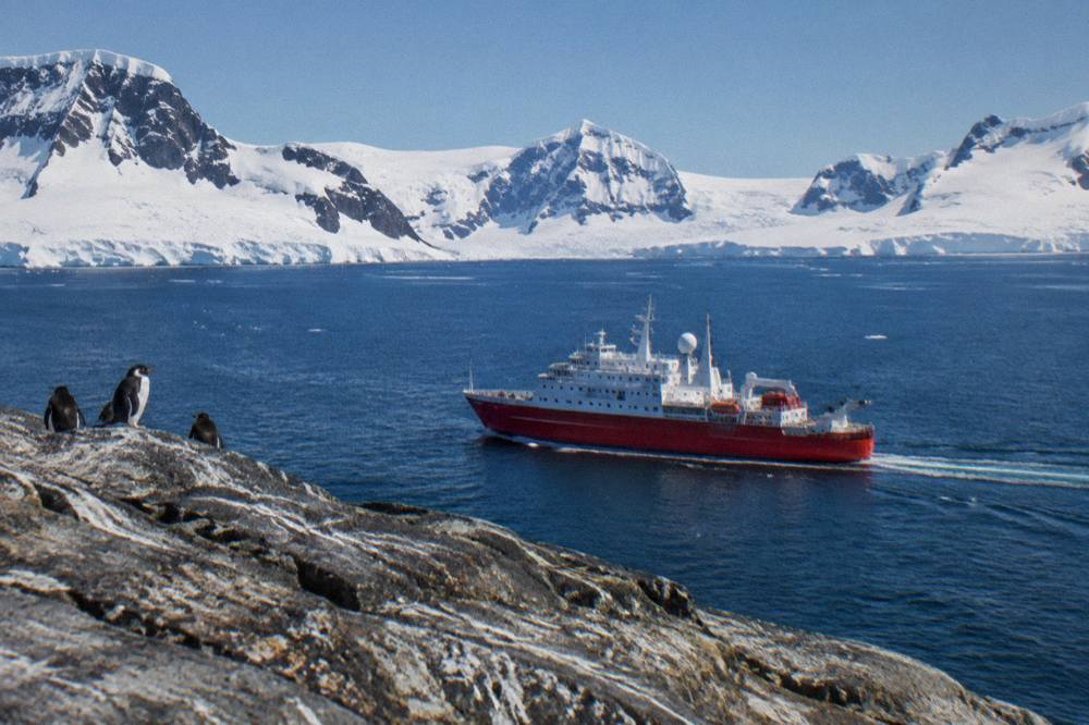 A small expedition ship sailing along a snow-covered Antarctic Peninsula coastline