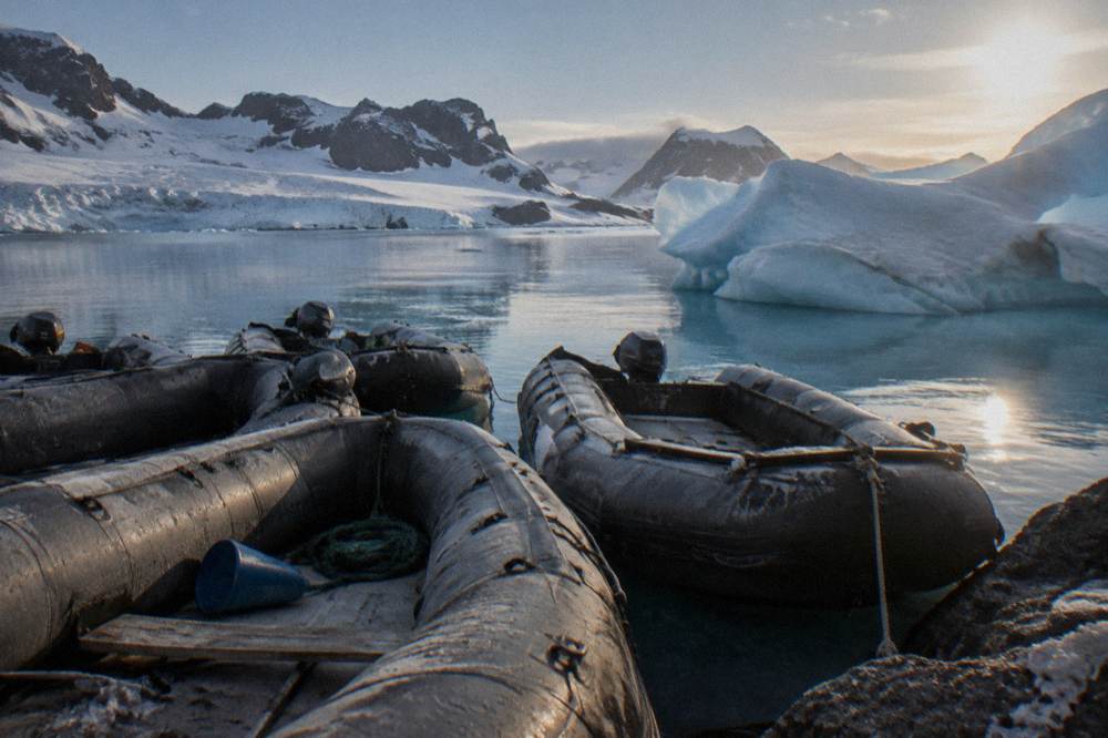 A line of Zodiacs tied together beside an iceberg in a calm Antarctic bay
