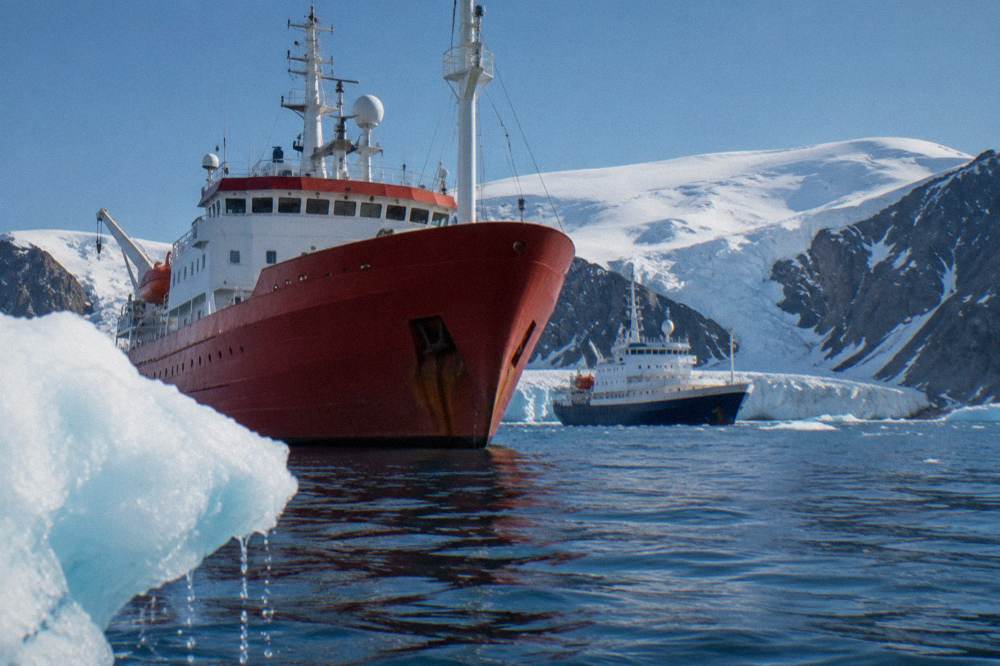 Two expedition ships anchored in a calm Antarctic bay under low light