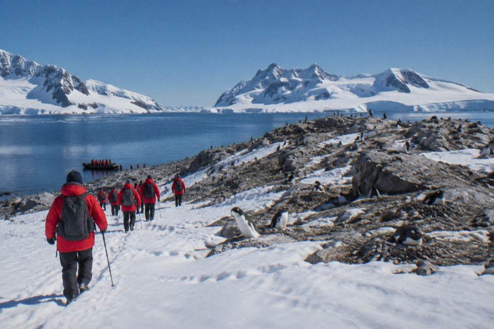 Passengers in red parkas walking up a snowy slope from a Zodiac landing site