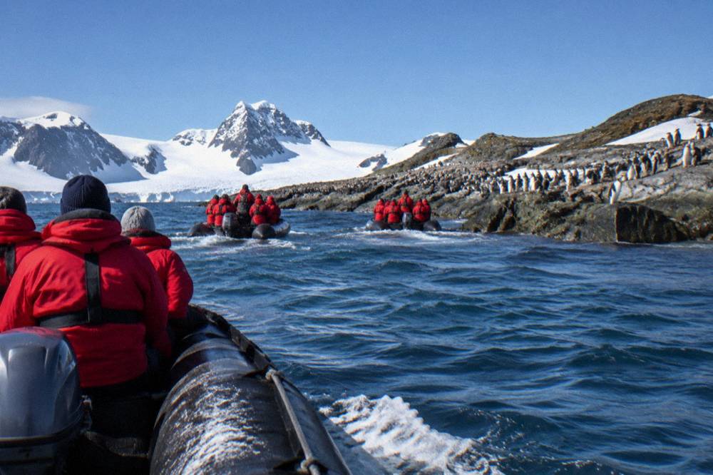 Zodiac boats carrying visitors toward a rocky Antarctic shoreline with penguins