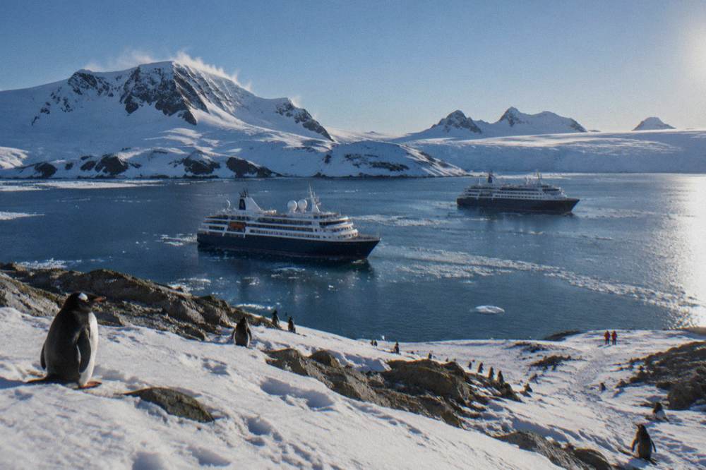 Two expedition ships at anchor in an Antarctic bay surrounded by sea ice