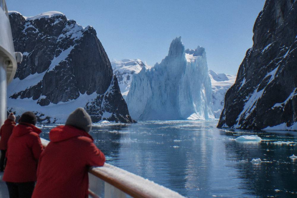 Passengers in red parkas watching icebergs from the observation deck of an expedition ship