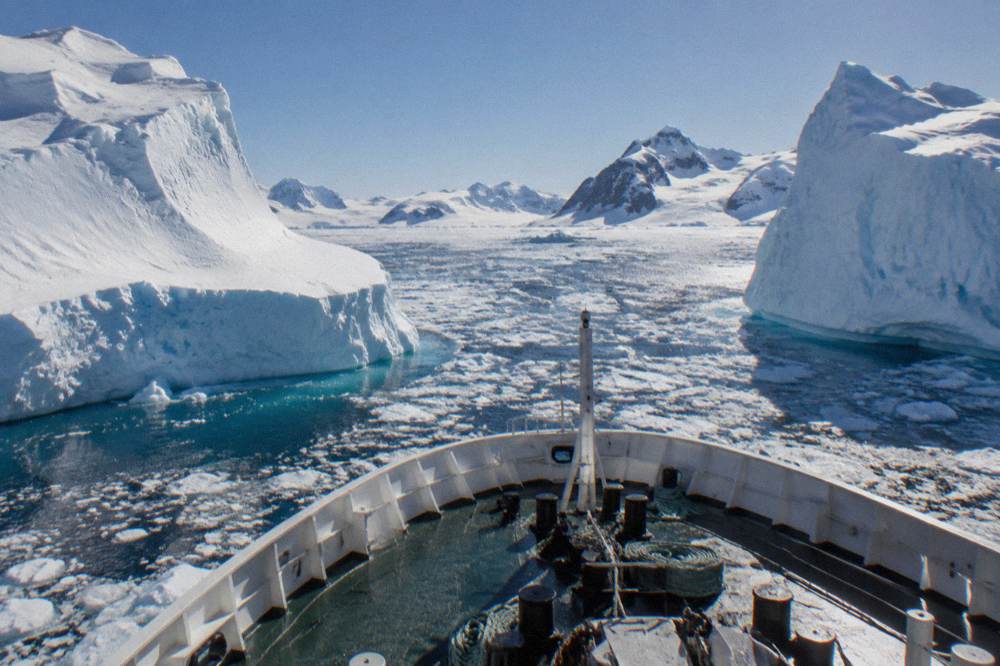 Expedition ship plowing through calm polar water between icebergs at dusk