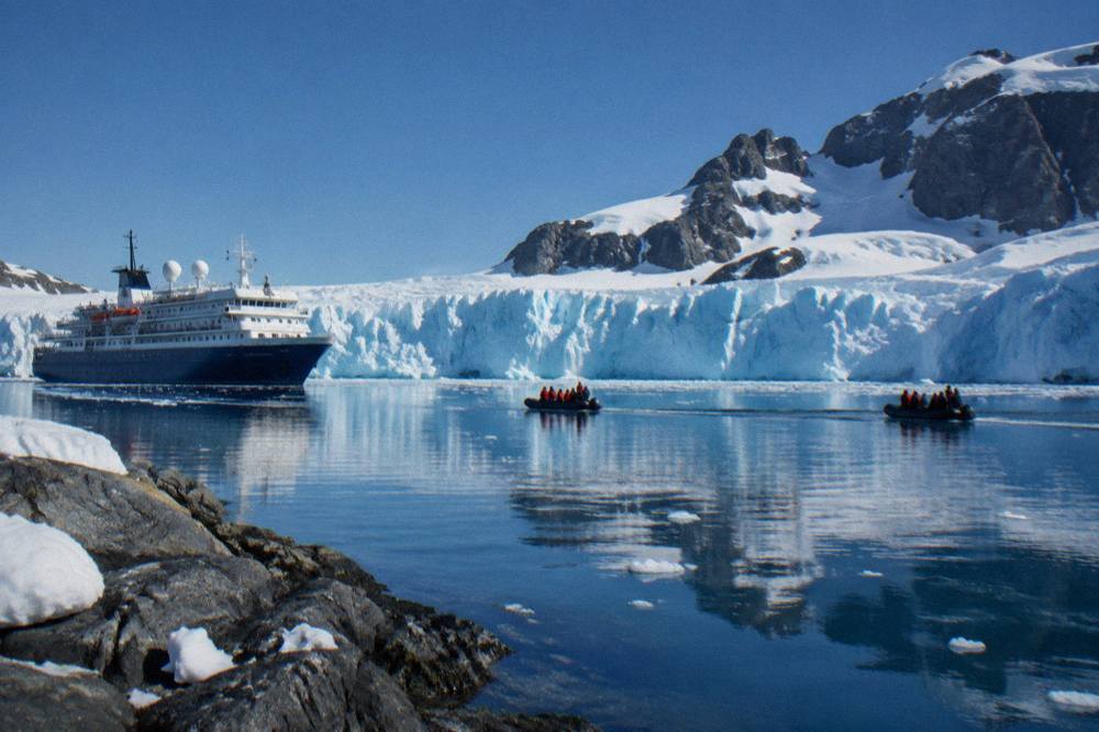 A polar expedition ship anchored near a glacier front with small Zodiac boats in the water