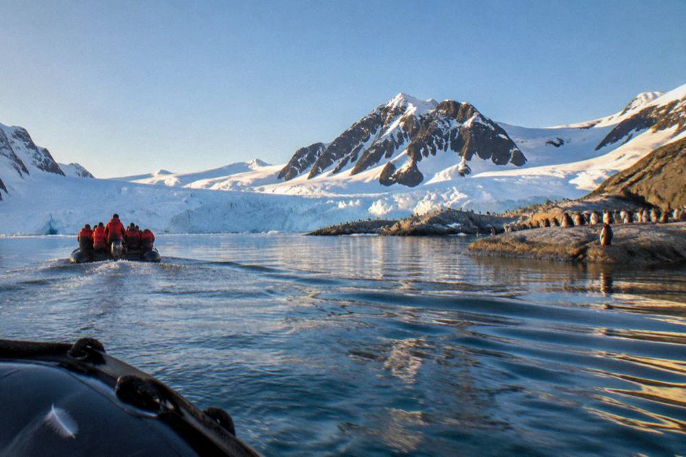 A Zodiac carrying red-jacketed passengers toward a glacier face in Antarctic waters