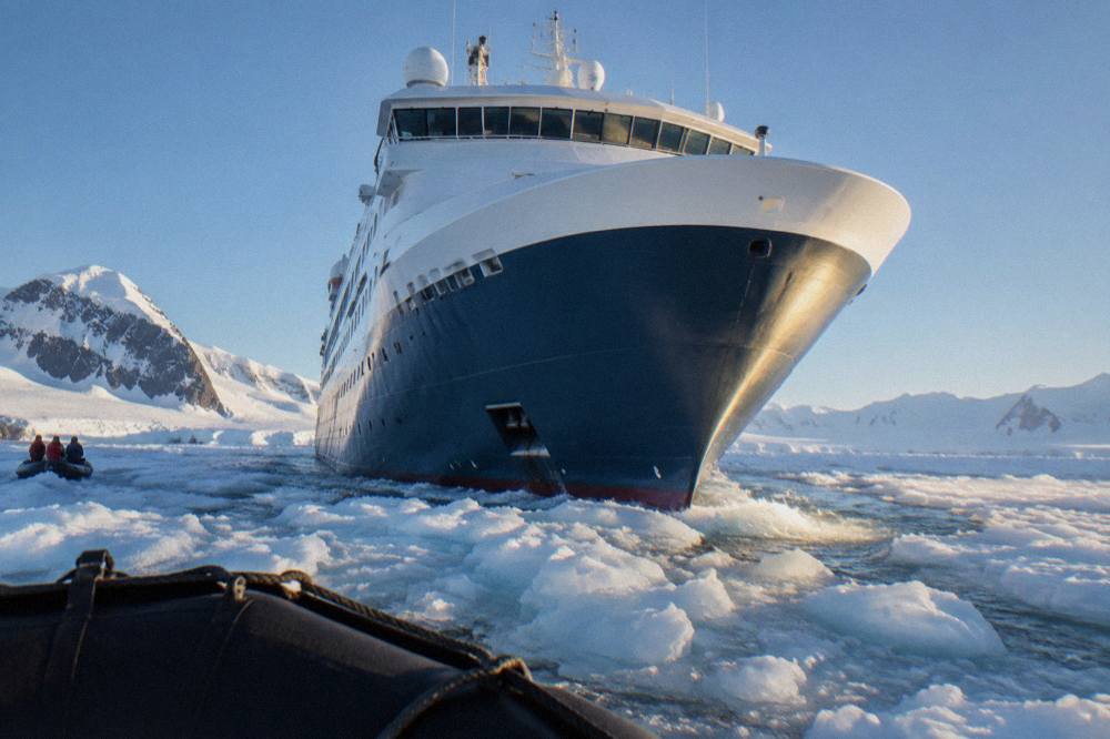 Expedition ship with a rounded X-Bow hull cutting through calm polar water near icebergs