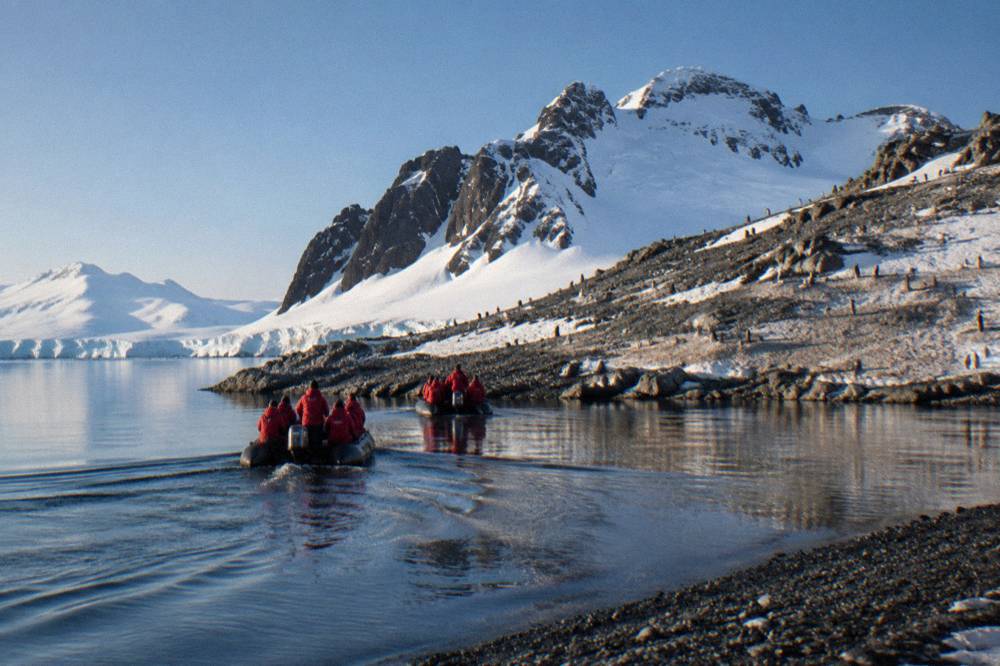 Zodiac boats carrying passengers toward a rocky landing site with penguins on the shore