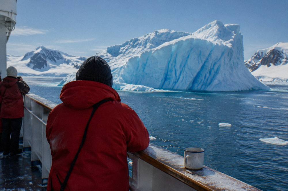 Passengers in parkas watching icebergs from the observation deck of a small expedition ship