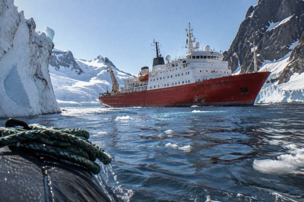 An expedition ship passing tall icebergs in a polar channel at dusk