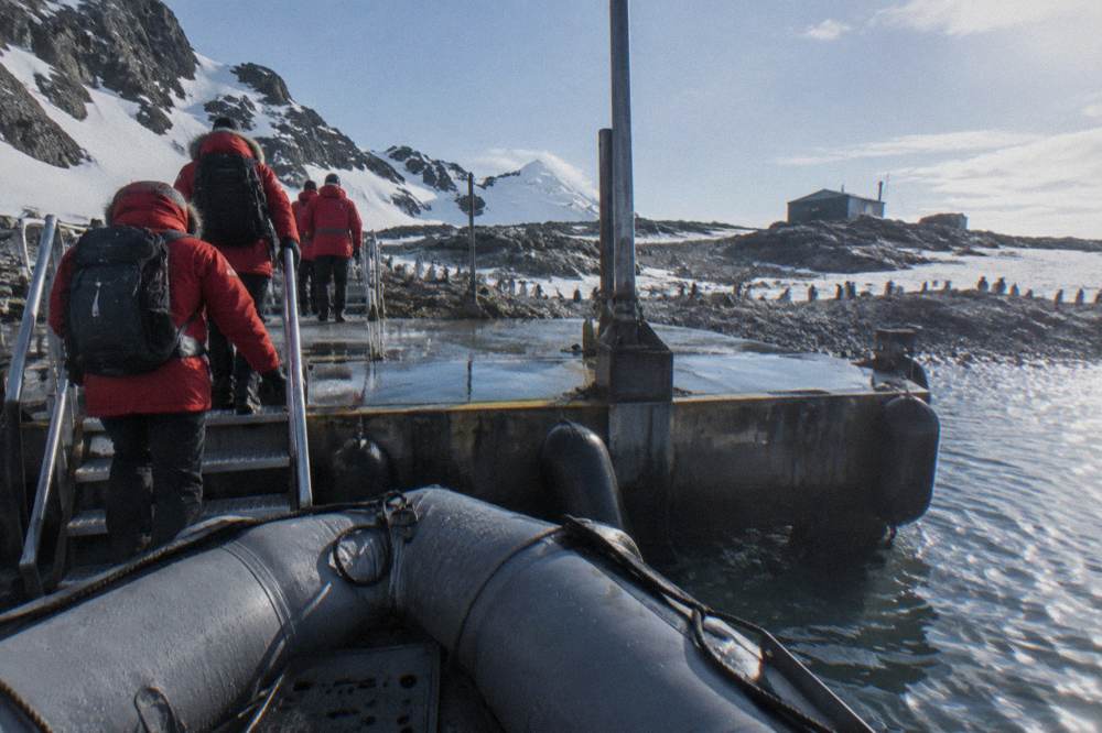 Travellers in red parkas boarding a Zodiac from an expedition ship gangway