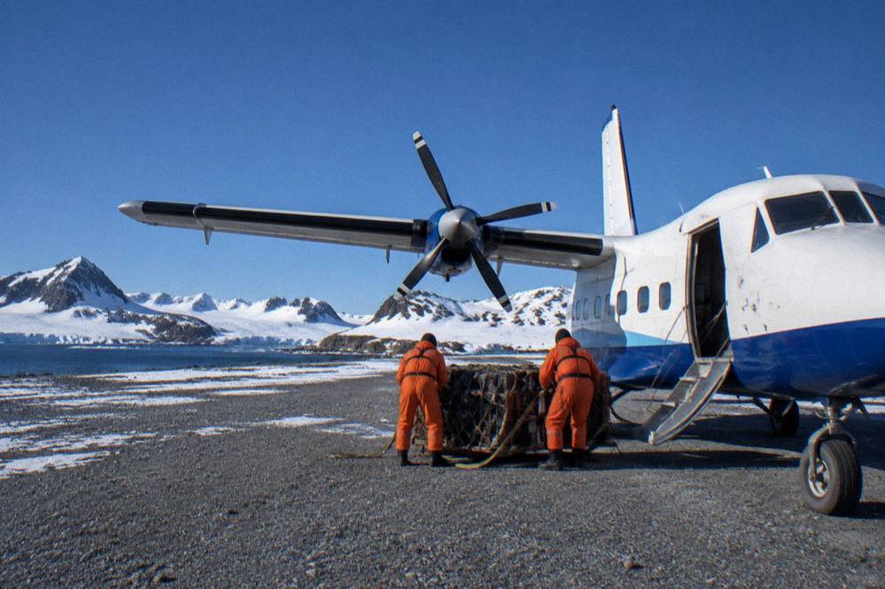 A twin-engine charter aircraft on a gravel airstrip surrounded by Antarctic snowfields