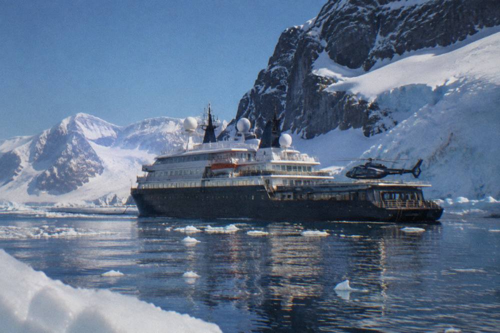 A dark-hulled luxury expedition ship at anchor near a glaciated Antarctic shoreline