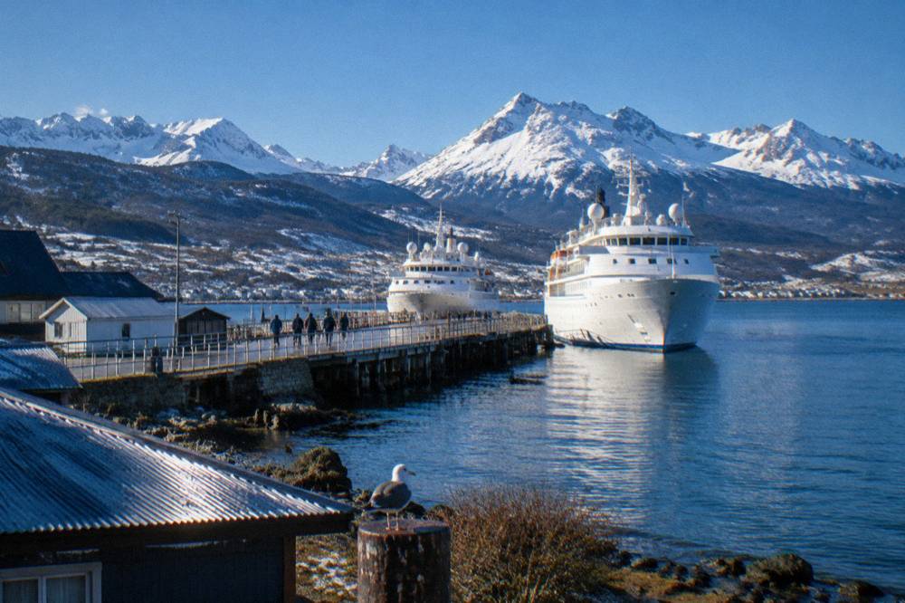 Two expedition ships moored at a wooden pier in a southern port town beneath mountains