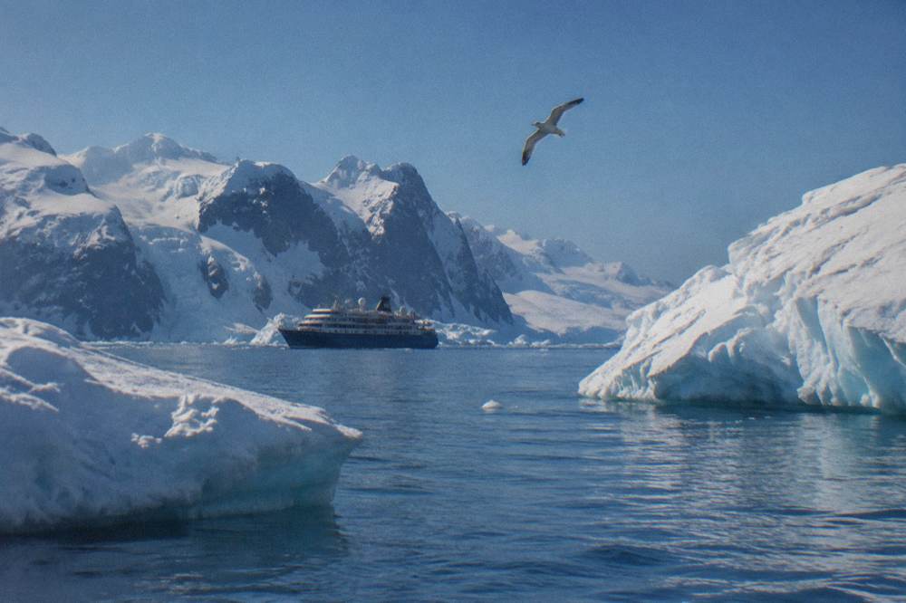 A small luxury expedition ship cruising between tall icebergs under a bright polar sky