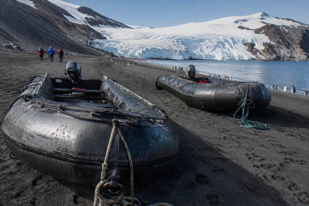 Two expedition ship tenders resting on a black volcanic beach beside a glacier