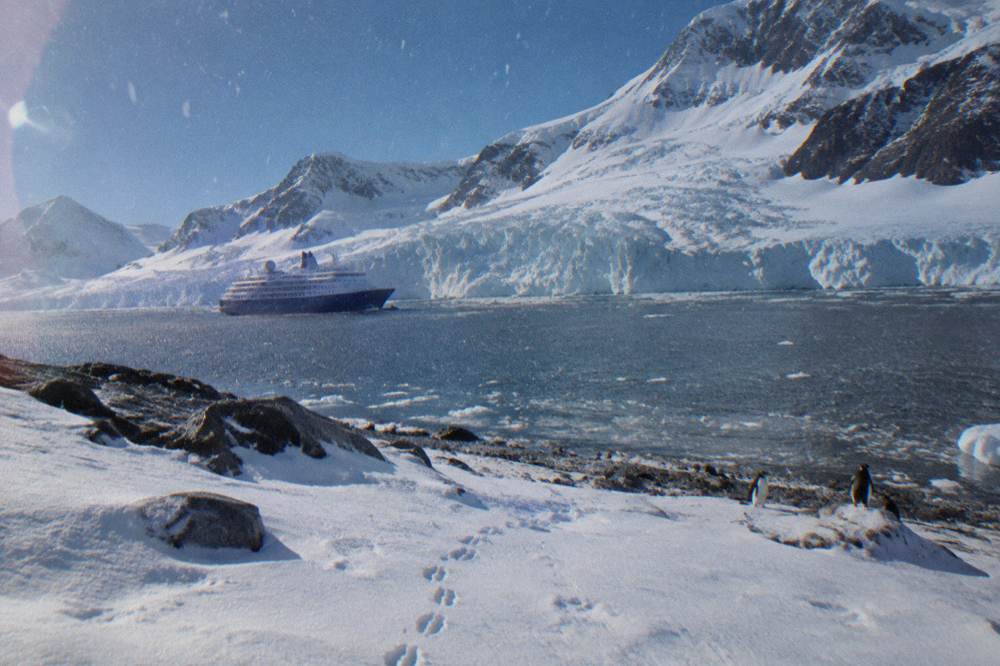 Luxury expedition ship at anchor near a glacier with snow-covered mountains behind