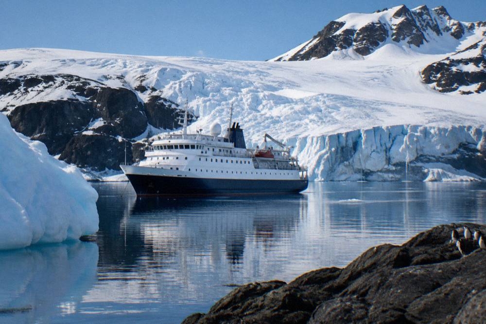 Expedition ship anchored near a snowy Antarctic peninsula shoreline