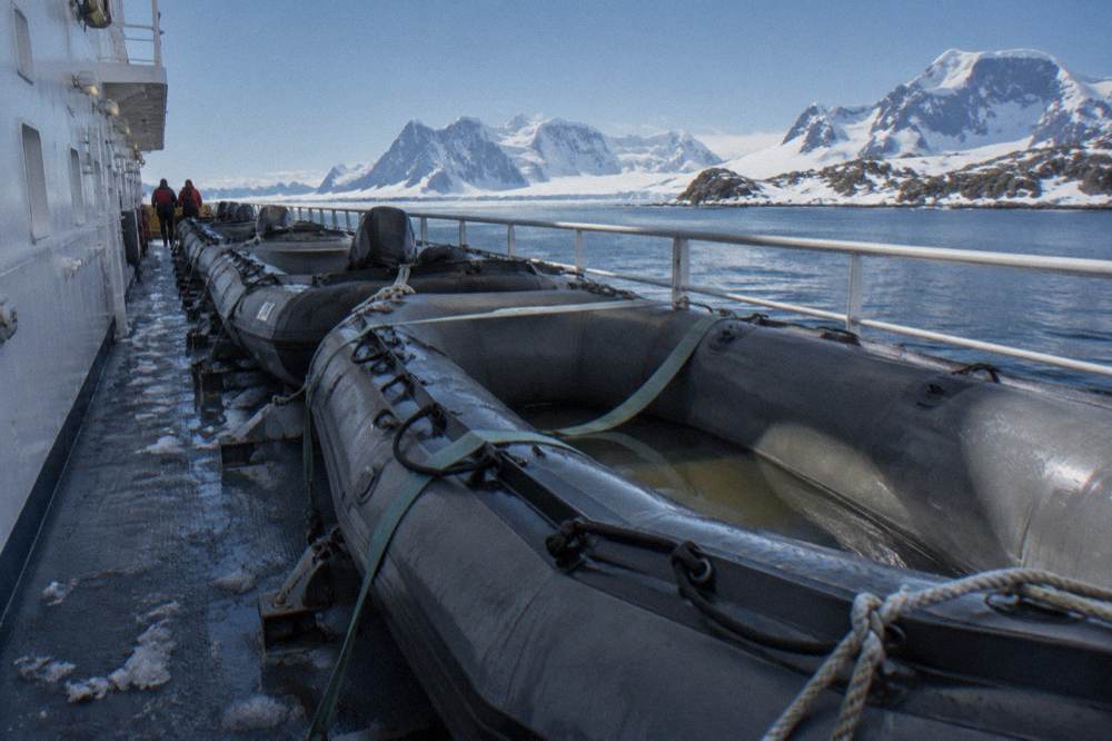 Zodiacs lined up on a ship deck beside a snowy coastline