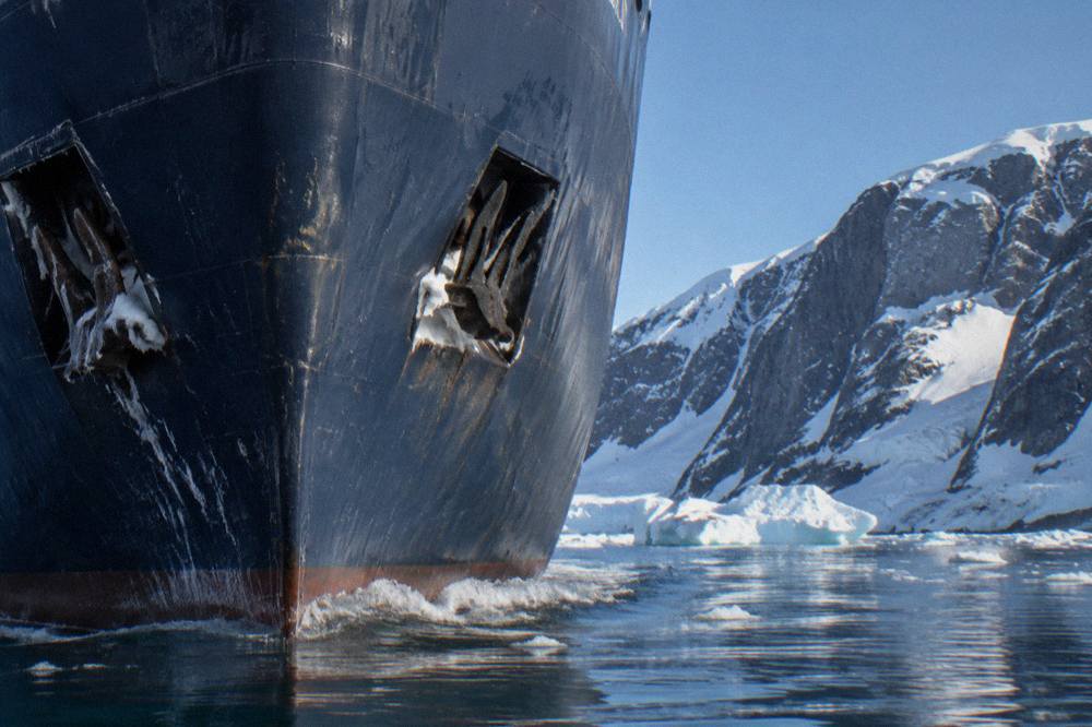 A polar expedition ship's bow cutting through calm icy water near icebergs