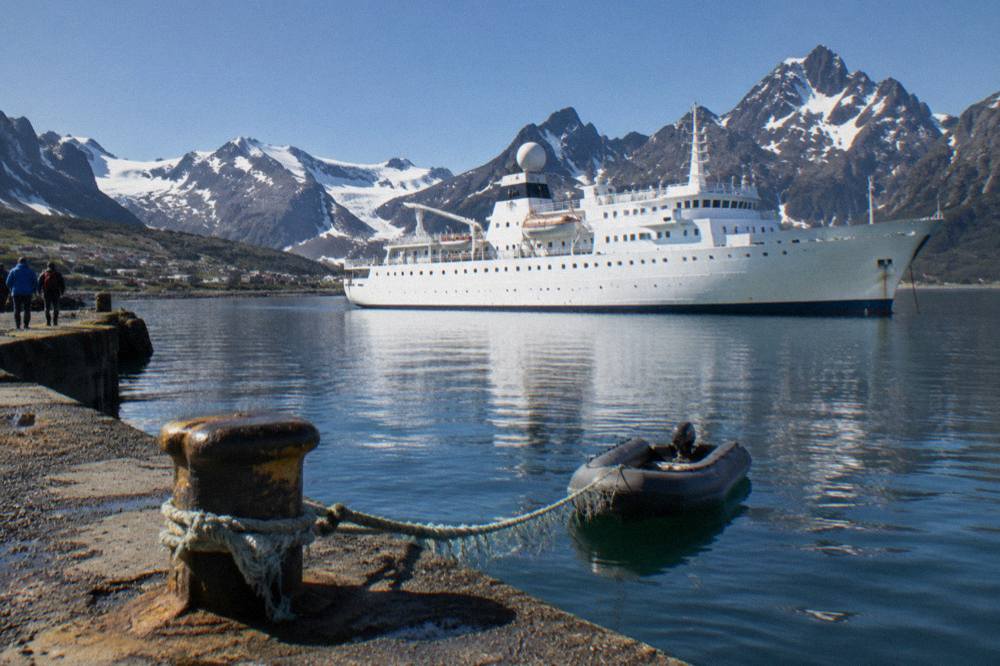 Expedition ship anchored in a calm Antarctic bay with jagged peaks behind