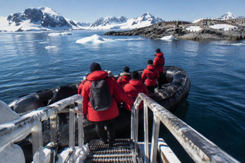 Guests in red expedition parkas boarding a Zodiac beside an ice-covered ship gangway
