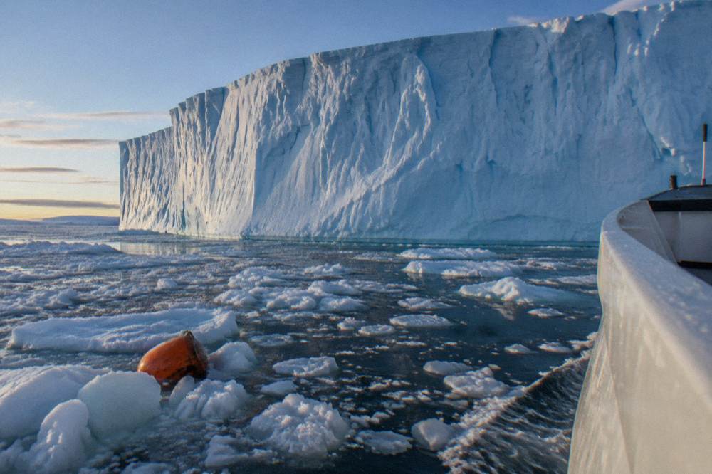 Luxury expedition ship cruising past a tabular iceberg under evening light