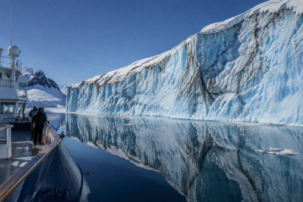 A luxury expedition ship with a dark hull cruising past a wall of Antarctic ice